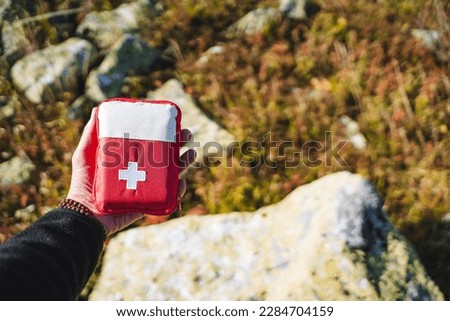 First aid kit, hand holding a first aid kit, a red bag with a white cross, an ambulance in the forest, camping equipment, a first-aid kit. High quality photo