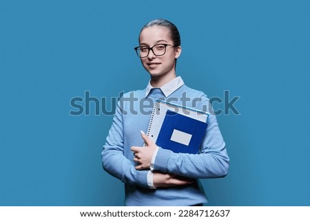 Portrait of smiling high school student girl with textbooks on blue background