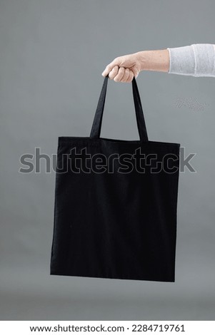 Hand of caucasian woman holding black canvas bag with copy space on grey background. Bags and fashion concept.