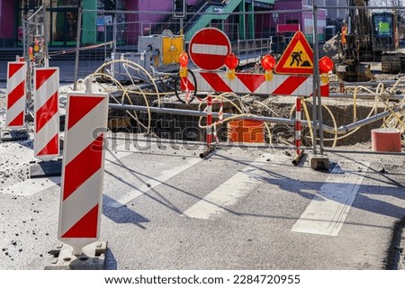 Street repair site with red and white striped vertical warning bollards, signs, barrier, temporary metal fence, repair pit dewatering system