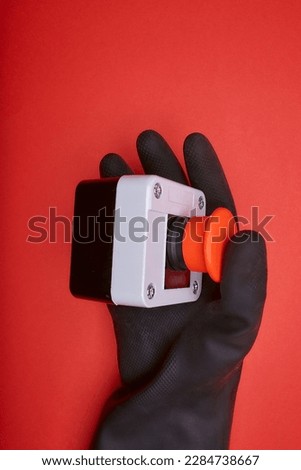 The hand in black resin glove, which pushes the emergency button at the red background at the side view
