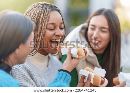 Three smiling friends eating hot dog in a park Royalty-Free Stock Photo #2284741243