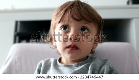 Toddler boy chewing food while watching media cartoon, infant child face staring