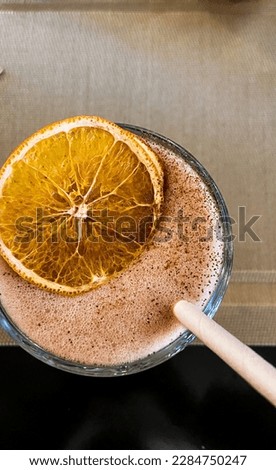 citrus coffee with milk shake, with a slice of dried orange and a paper eco straw.  top view, round glass