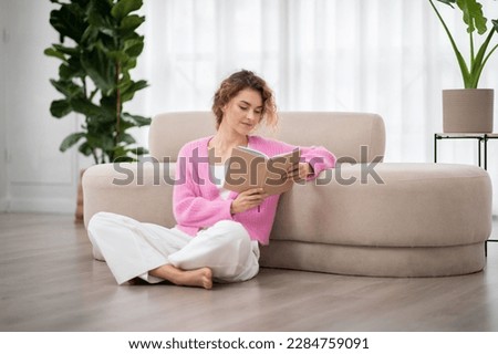 Portrait Of Beautiful Young Woman Reading Book While Relaxing At Home, Calm Millennial Female Sitting On Floor In Living Room And Enjoying Favorite Novel. Leisure, Literature And People Concept Royalty-Free Stock Photo #2284759091