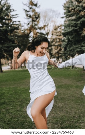 A bearded young groom and a beautiful smiling bride in a white brunette dress are hugging, dancing in a park outdoors. Wedding photography of happy, cheerful newlyweds, portrait.
