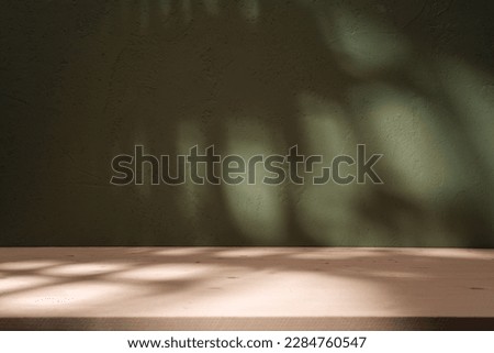 Empty table and darkgreen wall. Table with sun reflections and leaves shadows on beige wall. Background with bokeh for product presentation.Mock up for presentation, branding products, cosmetics food  Royalty-Free Stock Photo #2284760547