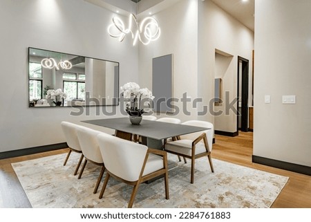 Elegant interior image of a dining room with black steel table soft tone curved back chairs swirling light fixture orchid and area rug contemporary home Royalty-Free Stock Photo #2284761883