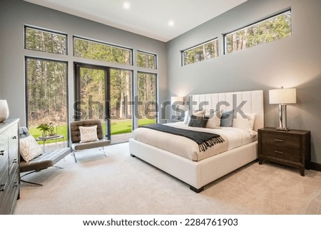 spacious elegant bedroom with stylish decor linens pillows soft color tones large windows with view to forest and patio Royalty-Free Stock Photo #2284761903