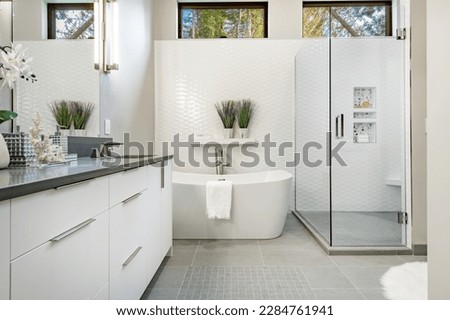 bright clean bathroom with white porcelain glass shower elegant tile grey cabinets basket weave tile on floor with access to laundry and walk in closet Royalty-Free Stock Photo #2284761941