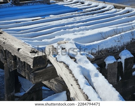 A snow covered plank stretching to an old bridge on a winter day.