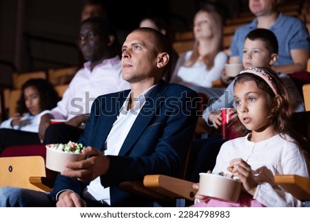 Father and daughter spending time together in cinema. Portrait of man with tween girl sitting in movie theater with popcorn and absorbedly watching film..