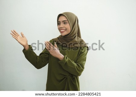 Smiling young Asian muslim woman in wearing casual clothes showing copy space on palm on white background. Ramadan Concept,