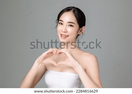 Young Asian woman short hair with natural makeup on face and clean fresh skin show Heart sign on isolated grey background. Portrait of cute female model in studio. Facial treatment, Cosmetology.