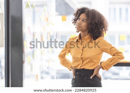 Young Asian woman Creative team use post it notes to share idea sticky note on glass wall. african business woman design planning and Brainstorming thinking sticky History notes concept.