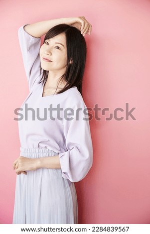 Portrait of a beautiful middle-aged Asian woman, standing in front of a pink wall. Beauty and Health Image.
