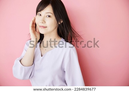 Portrait of a beautiful middle-aged Asian woman, standing in front of a pink wall. Beauty and Health Image.