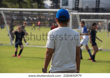 Soccer dads standing and watching his son playing football in a school tournament on a clear sky and sunny day. Sport, outdoor active, lifestyle, happy family and soccer mom and dad concept. Royalty-Free Stock Photo #2284850979