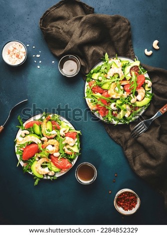 Two plates with salad with shrimps, avocado, grapefruit, arugula and cashews, table setting. Dark green background, top view Royalty-Free Stock Photo #2284852329