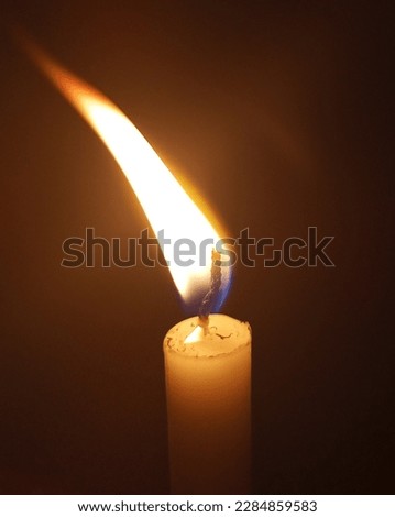 This photo shows the gentle flicker of a single candleflame, illuminating the darkness around it. The warm yellow light casts a soft, calming glow and creates a peaceful atmosphere. The flame is a sym