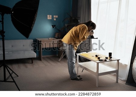 Woman in casual clothes using digital camera for making creative photos at home studio. Female photographer taking pictures of beauty skincare products on the table. Copy space