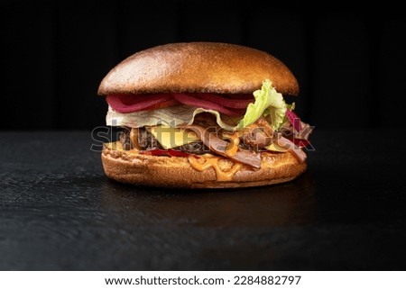 Cheeseburger with beef cutlet and cheese cheder on a black background, with greens