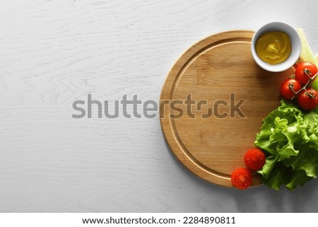 Food photography. Fresh cherry tomatoes, mustard and lettuce on white wooden table, top view with space for text