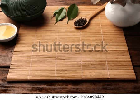 Bamboo mat, teapot, cup and spoon of dry tea leaves on wooden table, space for text Royalty-Free Stock Photo #2284898449
