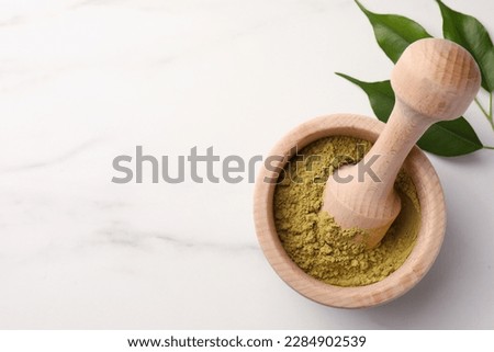 Mortar of henna powder and green leaves on white marble table, top view with space for text. Natural hair coloring Royalty-Free Stock Photo #2284902539