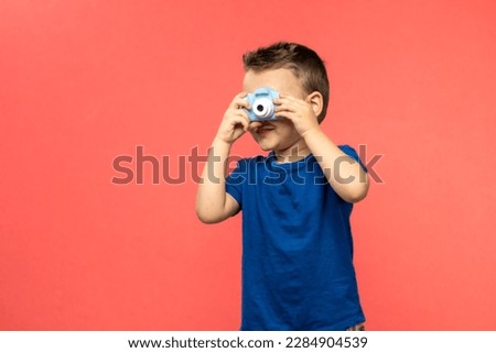 Little boy taking photo with kid film camera on coral background. Technology concept with copy space.