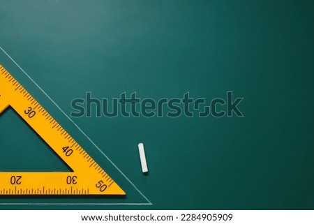 Yellow triangle and chalk on green chalkboard, flat lay. Space for text