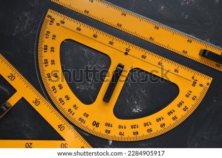 Protractor, ruler and triangle on blackboard, flat lay