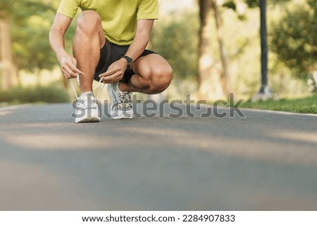 Young athlete man tying running shoes in the park outdoor, male runner ready for jogging on the road outside, asian Fitness walking and exercise on footpath in morning. wellness and sport concepts Royalty-Free Stock Photo #2284907833