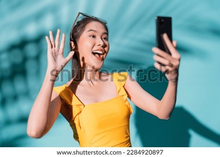 hello summer asia woman influencer in swimwear positive photo selfie using smartphone hand gesture action photo shoot with smile and happiness in summertime studio shot on blue colour background