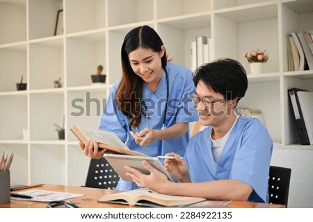Two smart young Asian medical students are discussing their medical cases and researching medical papers in a library together.