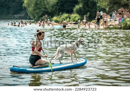 Snow-White Dog Standing on Sup Board, Woman Paddleboarding with Her Pet on City Lake. Sport and recreation theme