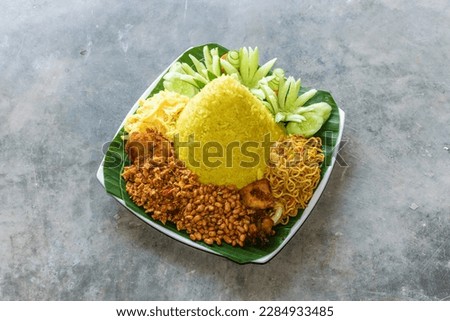 Yellow rice in a cone shape with noodles,  and sliced cucumber. In Indonesia called "Nasi Tumpeng" A Traditional Javanese Indonesian rice dish with side dishes
