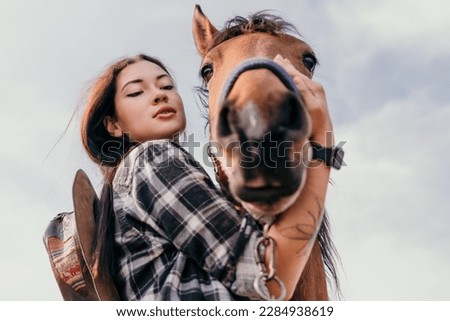 Young happy woman in hat with her horse in evening sunset light. Outdoor photography with fashion model girl. Lifestyle mood. Concept of outdoor riding, sports and recreation.