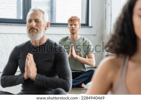 Redhead man meditating with anjali mudra near blurred people in yoga class Royalty-Free Stock Photo #2284940469