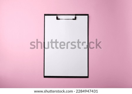 Black clipboard with sheet of blank paper on pink background, top view
