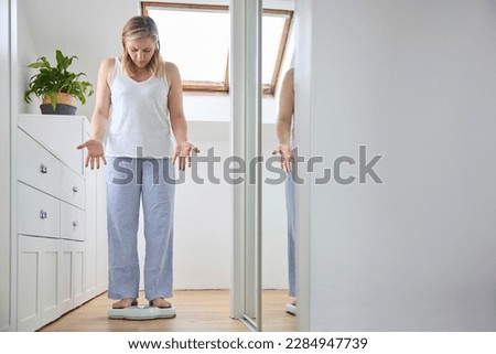 Menopausal Mature Woman Concerned With Weight Gain Standing On Scales In Bedroom At Home Royalty-Free Stock Photo #2284947739