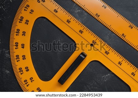 Ruler and protractor with measuring length and degree markings on blackboard, flat lay