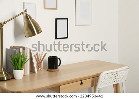Comfortable workplace with wooden desk near white wall indoors Royalty-Free Stock Photo #2284953441