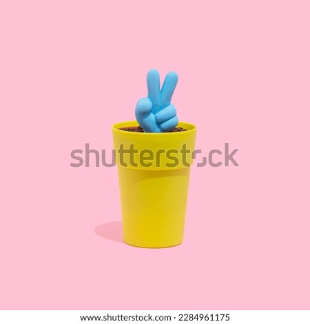 Blue peace, victory symbol icon growing from a small pot on a pastel pink background. Hand gesture, peace or victory concept.