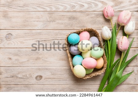 Happy Easter composition. Easter eggs in basket on colored table with yellow Tulips. Natural dyed colorful eggs background top view with copy space.