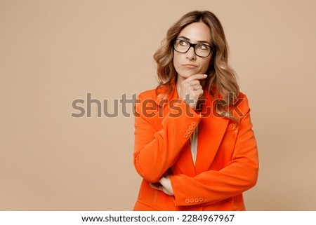 Young successful employee business woman corporate lawyer 30s wears classic formal orange suit glasses work in office prop up chin look aside on area isolated on plain beige color background studio Royalty-Free Stock Photo #2284967967