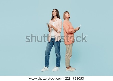 Full body fun happy elder parent mom with young adult daughter two women together wear casual clothes hold in hand mobile cell phone look overhead isolated on plain blue background. Family day concept Royalty-Free Stock Photo #2284968053