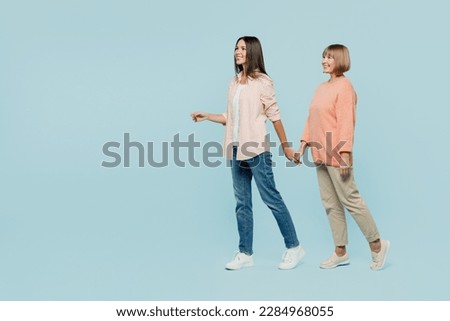 Full body side view happy fun elder parent mom with young adult daughter two women together wearing casual clothes hold hands walk go look aside isolated on plain blue background. Family day concept