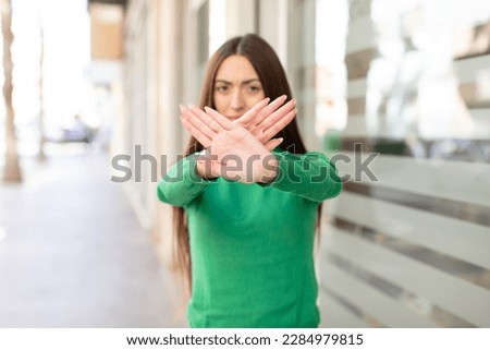 young pretty woman covering face with hand and putting other hand up front to stop camera, refusing photos or pictures