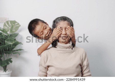 Surprise, close eyes, Asian grandson and grandmother people sitting together at desk.